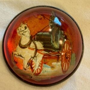 The 1930s to 1940s domed glass pin inside is a coach with horse and a rider.